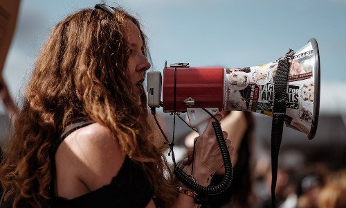 Woman with long hair holding bullhorn to her mouth.