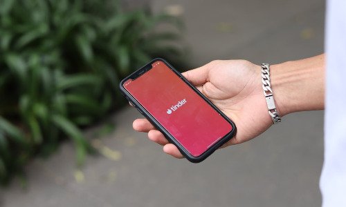 White hand holding cell phone with Tinder app logo on the screen.