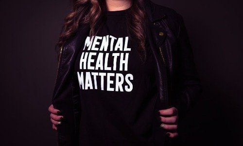 Hands holding a dark jacket open to show a black tshirt with the words Mental Health Matters in white letters