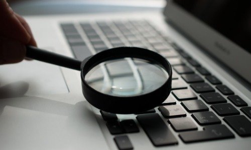 Magnifying glass with black handle held by a hand over a keyboard laptop
