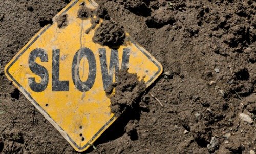 Yellow sign with Slow written in black letters, on the muddy ground.