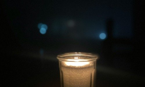 A single, white, candle burning in a glass jar.