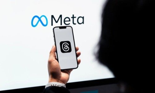 Meta logo on white background, with a hand holding a phone with the Threads logo on the screen.