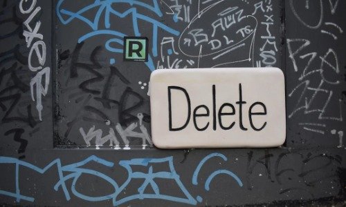 The word Delete on a sticker applied to a graffiti'd wall.