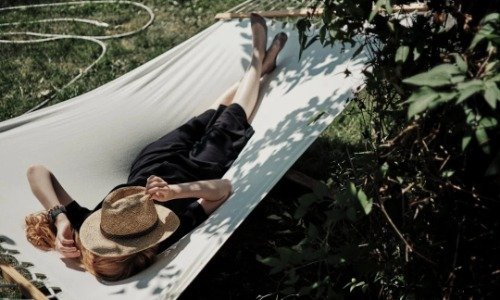 Woman in black dress with hat over her face laying in a white hammock